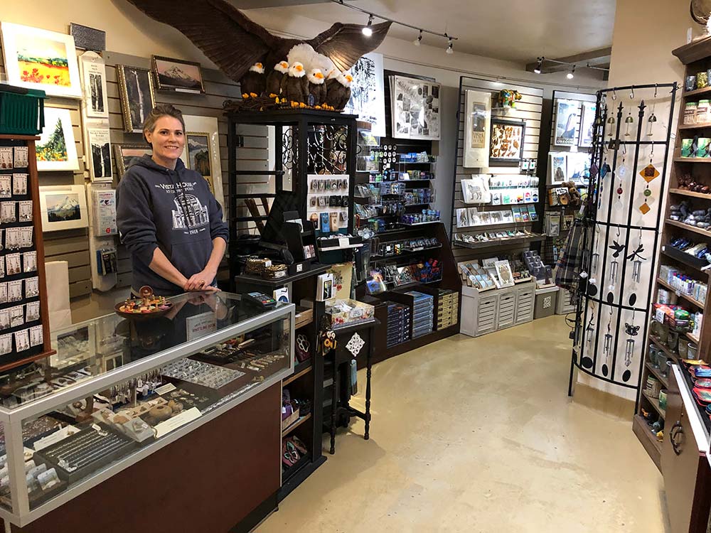 Image of the gift shop in the Vista House, containing various Pacific Northwest-themed memorobilia. A woman at the counter is smiling at the camera.